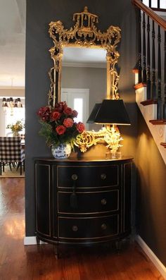 a black and gold dresser sitting under a mirror next to a stair case with flowers on it