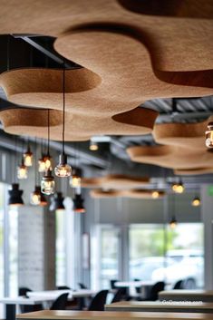 an empty restaurant with wooden tables and lights hanging from it's ceiling, in front of large windows