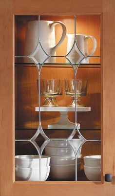 glass shelves with dishes and cups on them in a kitchen cabinet, showing the reflection of two mugs