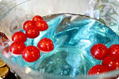 red cherries are floating in a bowl of water with gold coins around it and on the table