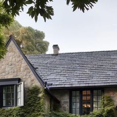 a stone house with black shutters and ivy growing on the windows, in front of a tree