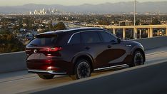 the rear end of a red mazda cx - 5 driving on a highway in front of a cityscape