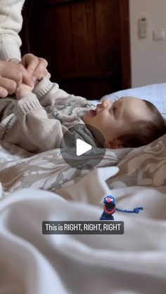 a baby laying on top of a bed next to an adult holding it's hand