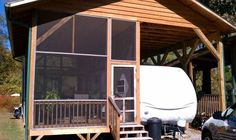 a small house with a covered porch next to a parked car and a white trailer