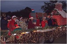 people dressed as santa clause riding in the back of a truck decorated with christmas lights