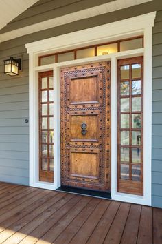 a wooden door sitting on the side of a gray house next to a light fixture