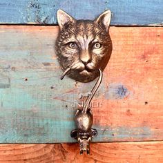 a metal cat head mounted to the side of a wooden wall next to a hook