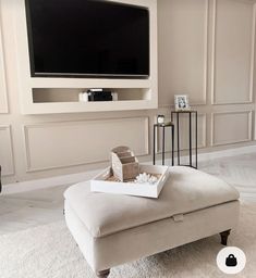 a living room with a large flat screen tv on the wall and white rugs