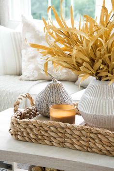 a wicker basket with a candle, vase and sea urn sitting on a coffee table