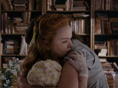 a woman with red hair hugging another woman in front of a book shelf filled with books