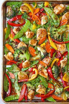 a sheet pan filled with chicken, peppers and broccoli covered in sesame seeds