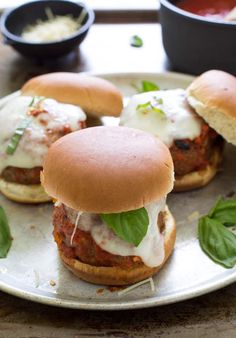 two meatball sandwiches with cheese and basil on a silver plate, ready to be eaten