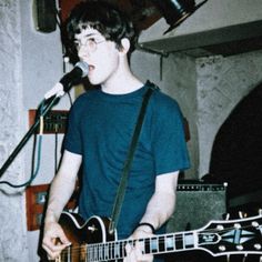 a young man singing into a microphone while playing an electric guitar in front of him