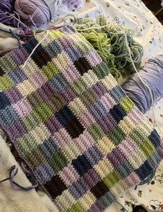 yarns and knitting needles are laying on a bed with a crocheted blanket