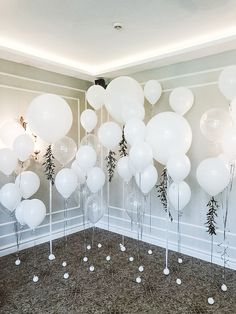 white balloons and greenery are arranged in the corner of a room