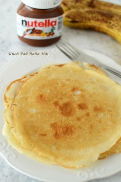 two pancakes on a plate with peanut butter and a banana in the backgroud