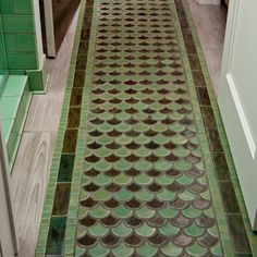 a long hallway with green and brown tiles on the floor next to a white door