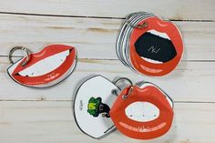 three red lips shaped key chains on top of a white wooden table with two tags attached to them