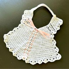 a white crocheted baby bib with pink ribbon hanging from it's neck