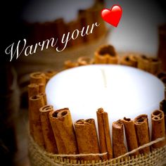 a white candle with cinnamon sticks around it and the words warm your heart on top