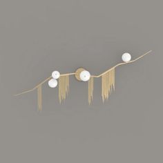 three white balls hanging from a string on a gray wall with gold fringes and beads