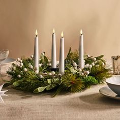 a table topped with candles and greenery on top of a white plate next to a bowl