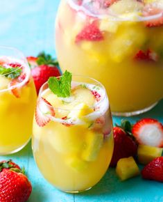 two glasses filled with lemonade and strawberries next to some sliced pineapples