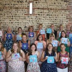 a group of women standing next to each other holding up some artwork on their hands