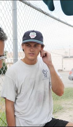 a man sitting on the ground talking on his cell phone next to a chain link fence