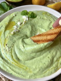 a hand dipping a piece of bread into a bowl of green guacamole