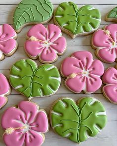 decorated cookies with pink, green and white icing on a wooden table next to leaves