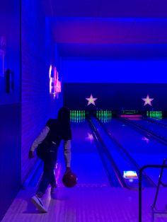 a bowling alley is lit up with purple lighting and stars on the wall, while a person holds a basketball in his hand