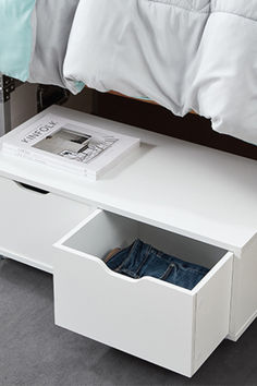 a white bed with an open drawer underneath it and a book on the bottom shelf