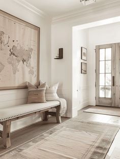 a large map hangs on the wall above a bench in a white room with wood floors