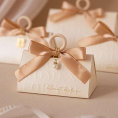 two white boxes with gold ribbons tied around them and one has a ring on it