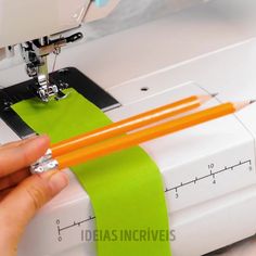 a person using a sewing machine to sew on a green piece of paper with two orange pencils