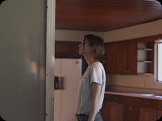 a woman standing in a kitchen next to an open door and looking at the floor