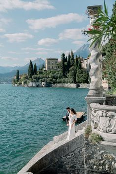 a man and woman standing on the edge of a pier next to a body of water