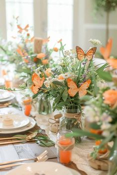 the table is set with orange and white flowers in mason jars, silverware, and candles