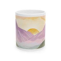 a coffee mug with mountains painted on the side and sun in the distance behind it