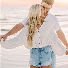 a man and woman walking on the beach holding each other's hands as they laugh