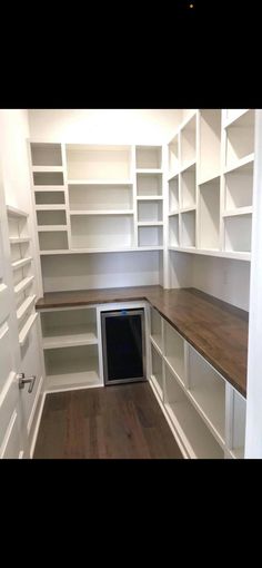 an empty room with white shelves and wood flooring in the center is a wine cellar built into the wall