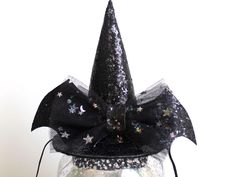 a black witch hat with stars and sequins on the top is sitting in a glass jar