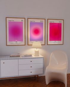 a white chair sitting next to a lamp on top of a wooden floor in front of two posters