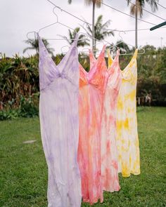 three dresses are hanging on a clothes line in the grass, with palm trees in the background