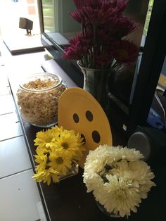 flowers and plates on a table in front of a television with a smiley face painted on it