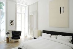 a white bedroom with a black chair and large painting on the wall in front of it