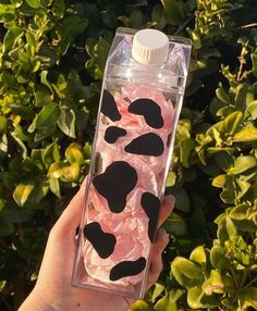 a hand holding a water bottle filled with pink and black liquid in front of bushes