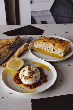 two white plates with food on them sitting on a table next to utensils