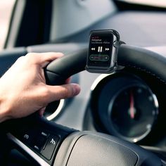 a person is holding an apple watch in their hand and driving a car with the other hand on the steering wheel